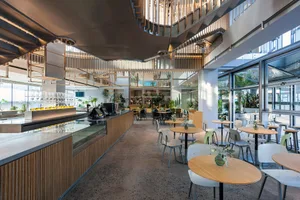 Open modern restaurant with wood flooring, multiple dining tables, and a bar area, well-lit for a welcoming atmosphere