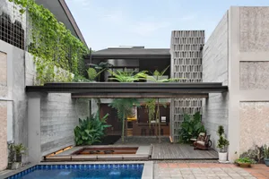 A modern house with a pool and a large window, surrounded by potted plants and two chairs for relaxation