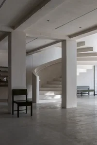 Open minimalist space with a spiral staircase, two benches, and a chair, featuring clean lines and a central staircase