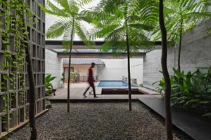 A serene outdoor living space with a pool surrounded by lush tropical plants and a man walking on the patio