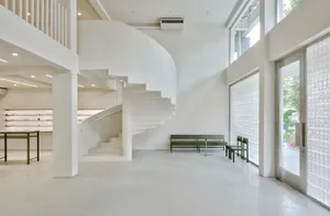 Empty minimalist room with a spiral staircase made of concrete and metal railing, surrounded by white walls and floor