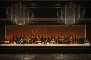 A sophisticated bar area with a long wooden counter featuring numerous bottles of liquor and two wine glasses, set in a warm and inviting environment