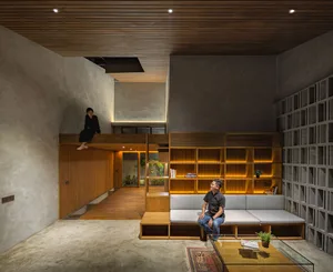 A modern open concept living area with two men sitting on couches, surrounded by chairs, a potted plant, and books, creating a comfortable and inviting atmosphere