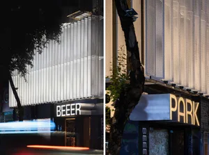 A modern building with a large glass wall and trees in the background, set against a blurred urban environment