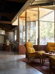 A modern living room with a yellow chair, dining table, couches, and a potted plant, well-lit by natural sunlight