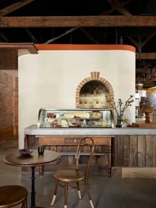 Warm and inviting cafe interior with a wooden counter, display case, and dining table, featuring a cozy atmosphere and natural materials
