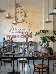 Warm and inviting coffee shop interior with tables, chairs, potted plants, artwork, and a painting of a woman holding a cup