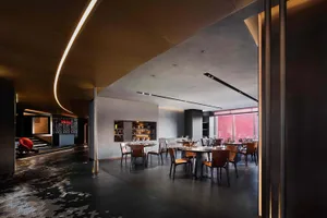 A modern dining area with multiple tables and chairs, well-lit by natural and artificial light, featuring wine glasses and a sophisticated atmosphere