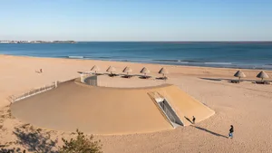A modern beachside restaurant with a large dome structure housing several umbrellas, surrounded by a beautiful ocean view