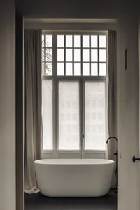 A calm bathroom with a white bathtub next to a window covered in curtains