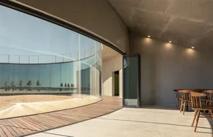 A relaxing indoor space with a large glass wall offering a view of the beach, wooden flooring, and natural light