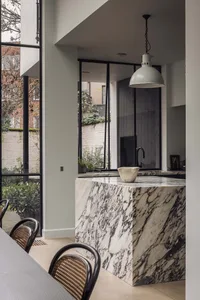 A modern kitchen with a marble countertop island, chairs, and a sink, featuring a cozy dining setup and elegant atmosphere