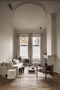 Modern living room with a white interior, wood furniture, and a fireplace, featuring two windows and a clean, bright atmosphere