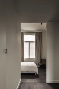 A calm bedroom with a white bed in front of a large window, two chairs, and a couch, with a focus on simplicity and functionality