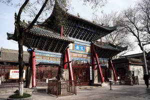 Asian-style building with red walls, a large gate entrance, and several statues, including a lion, set against a cultural and artistic backdrop