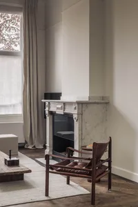 Cozy living space with a fireplace mantel, two chairs, and natural light from windows