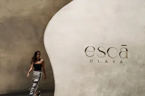 A woman in a black dress walks past a wall with an advertisement for Escapade Playa in a modern and stylish hotel lobby