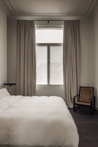 Cozy bedroom with a white bed, two chairs, and a dining table, featuring a clean and inviting atmosphere