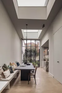 Open living area with white walls, large window, natural light, chairs, couch, dining table, decorative elements, and potted plants