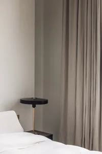 A cozy bedroom with a white bed, a black and gold lamp on each side, and a chair near the foot of the bed