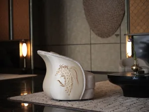 A well-lit living room with a white chair featuring gold accents and a dragon design, in front of a table, with a vase suggesting decorative elements