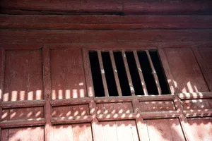 Old red building with a window featuring bars, set against a warm and inviting background