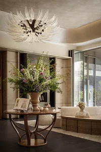 A well-lit living area with a wooden table, couch, and vase with flowers, surrounded by scattered books, creating a warm and inviting atmosphere