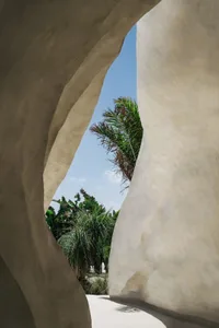 A modern space with a large white wall featuring a hole for a unique view of the surrounding tropical landscape with palm trees