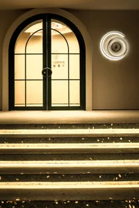 A bright and welcoming entrance with a green door and white wall, illuminated by two circular lights