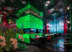 Modern restaurant interior with green walls, bar area, dining tables, chairs, vases with flowers, and bottles