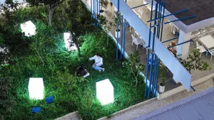 A serene indoor garden with grass, trees, and plants, featuring two people sitting on the grass, surrounded by lush greenery and artificial lighting