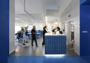 Casual restaurant interior with a blue countertop, blue walls, and modern blue tiles, featuring a bustling atmosphere with people ordering food