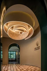 A hotel lobby with a circular ceiling light fixture, chairs, and a potted plant, creating a warm atmosphere