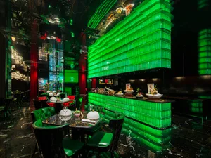 Modern restaurant bar with green walls, white tables, and chairs, featuring white bowls and a stylish atmosphere