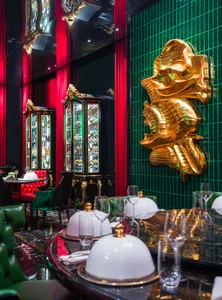 Luxurious dining area with a gold statue centerpiece, red leather chairs, and wine glasses on a table surrounded by books