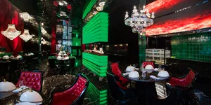 Sophisticated restaurant interior with green walls, black chairs, and tasteful decor, featuring multiple dining tables and wine glasses