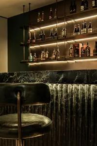 A sophisticated bar area with a black leather chair, marble countertop, and a selection of bottles on display