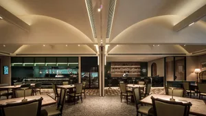 A lively restaurant interior with multiple tables, chairs, and decorative items such as bottles, vases, and potted plants, set in a modern and stylish environment