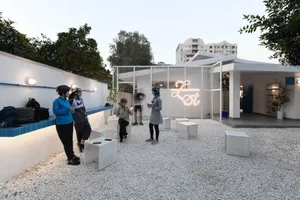 A modern indoor space with white walls, hosting a social gathering with several people standing and interacting