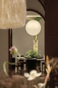 Dining area with a round table, chairs, wine glasses, and a vase, set in a well-lit room with a warm and inviting atmosphere