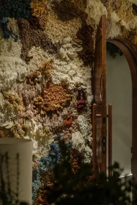 A fabric wall display with plants and wood elements, featuring potted plants and wooden doors in the background