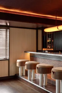 A bar area in a restaurant with a long wooden counter and stools, featuring an inviting and comfortable atmosphere