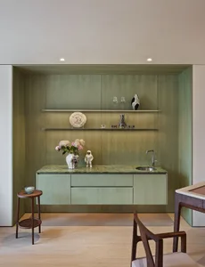 Cozy kitchen with green cabinets, marble countertop, and two chairs, featuring wine glasses, a vase, and a bowl on the counter