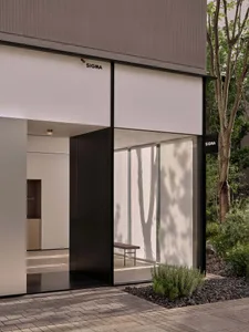 A modern building with a black door and white wall, surrounded by trees, featuring a glass door and window