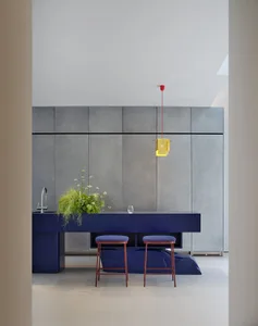 Modern kitchen with a blue countertop, grey walls, a sink, stools, and a potted plant