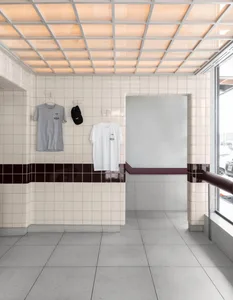 A bathroom or locker room with white t-shirts on hooks, tile walls, and a background of multiple cars suggesting a location near a parking lot or busy street