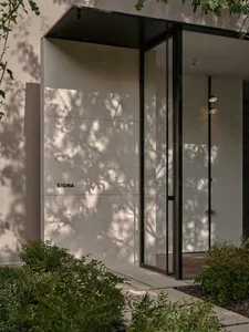 A white building with a glass door and window, surrounded by potted plants, with bright and inviting sunlight streaming through the windows