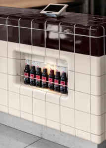 A kitchen with a white tile wall featuring a vertical display of various soda bottles, creating a clean and organized space