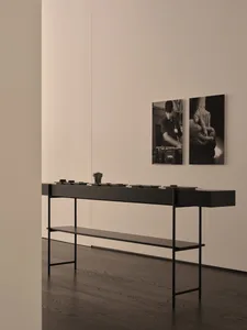 A white room with a black table and artwork on the walls, including a portrait of a man, with a bowl and vase on the table