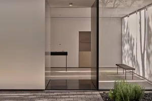 A modern kitchen or living area with white walls, large windows, and a bench, featuring a clean and bright appearance with ample natural light